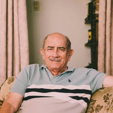 A cheerful elderly man enjoys a relaxed moment on a sofa in a warmly decorated living room.