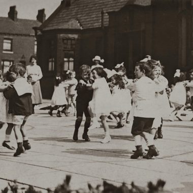 Children dancing in a school playground in a vintage black and white photo.